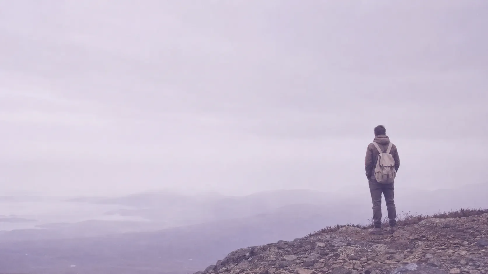 A traveler with a backpack looking out over snow-capped mountains at sunrise